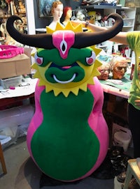 a woman is standing next to a large green and pink monster